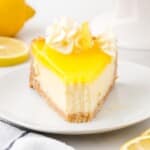 A high-resolution shot of a slice of lemon cheesecake with a bite on a fork, lemon curd topping, whipped cream, and fresh lemon in the background.