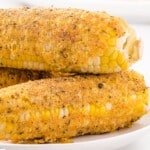 Fried corn on the cob on a white plate with a label saying "Fried Corn on the Cob with thick and creamy batter!"