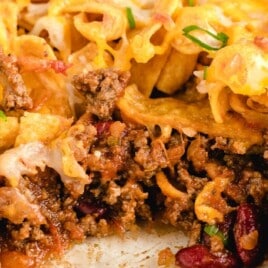 A close-up of a cheesy, baked Frito pie with crispy corn chips, melted cheese, and a hearty beef and bean filling inside a glass baking dish.