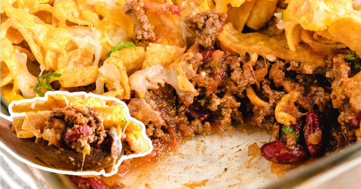 A large baking dish of Frito pie half-eaten, showing the beefy interior, beans, and gooey cheese with a scoop highlighted in a corner.