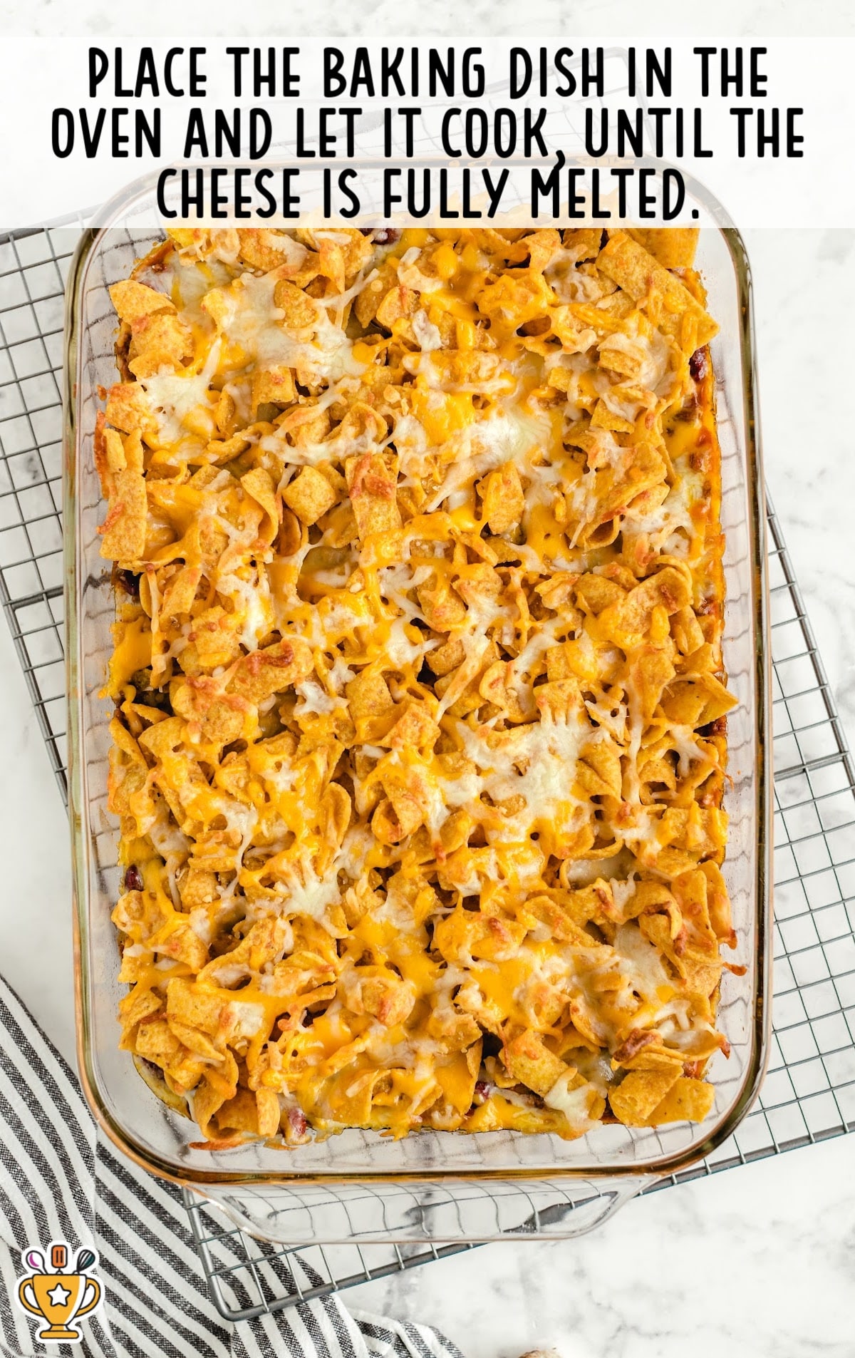 Freshly baked Frito pie in a glass baking dish on a cooling rack, showing melted cheese and golden corn chips.