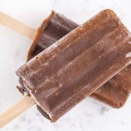Four chocolate fudgesicles lined up with one bitten, set against a white background and outlined for emphasis.