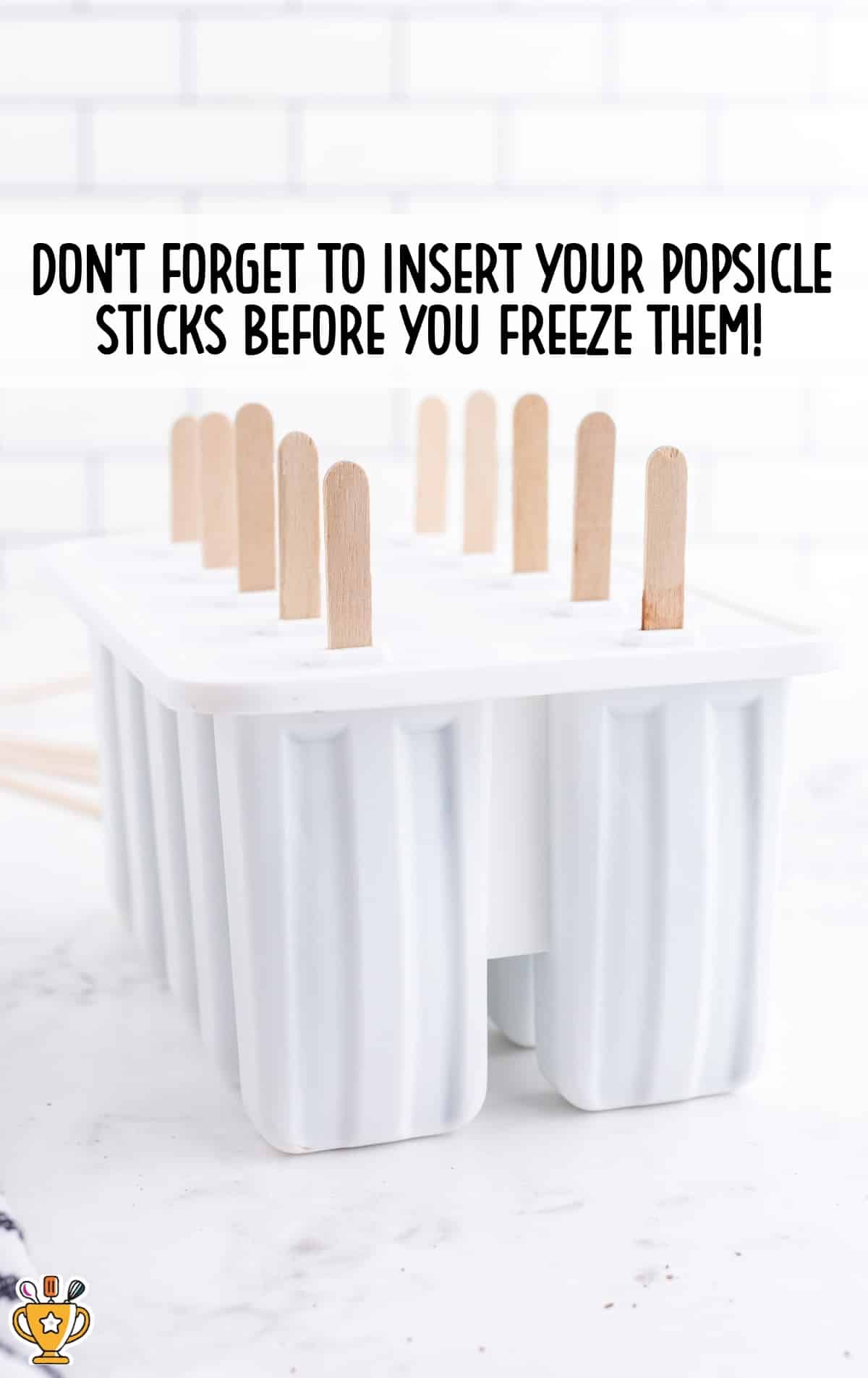 Popsicle sticks inserted into filled molds before freezing, with a clean white kitchen background.