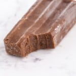 Fudgesicle ingredients listed over the popsicles, including pudding mix, milk, popsicle sticks, and molds on a white background.