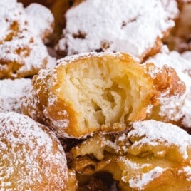 Square image of golden funnel cake bites dusted in powdered sugar, highlighting the texture of the fried dough and soft inside.