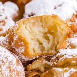 Close-up of golden funnel cake bites dusted in powdered sugar, with one bite showing the fluffy interior texture.