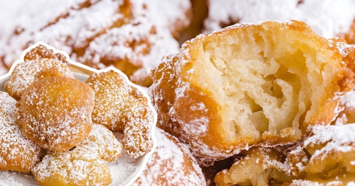 A pile of freshly fried funnel cake bites with a cut-open center showing a soft interior, and a bowl of more bites on the side.