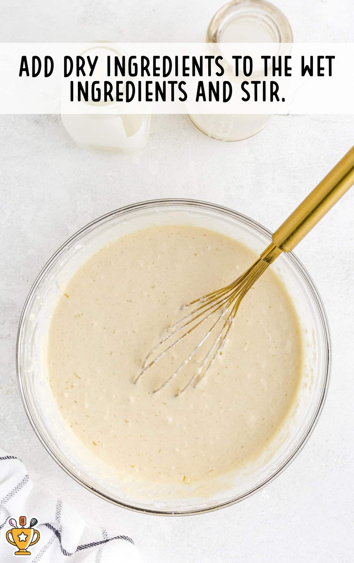 Bowl of mixed funnel cake batter with a whisk, ready for frying, placed on a white surface next to a striped towel.