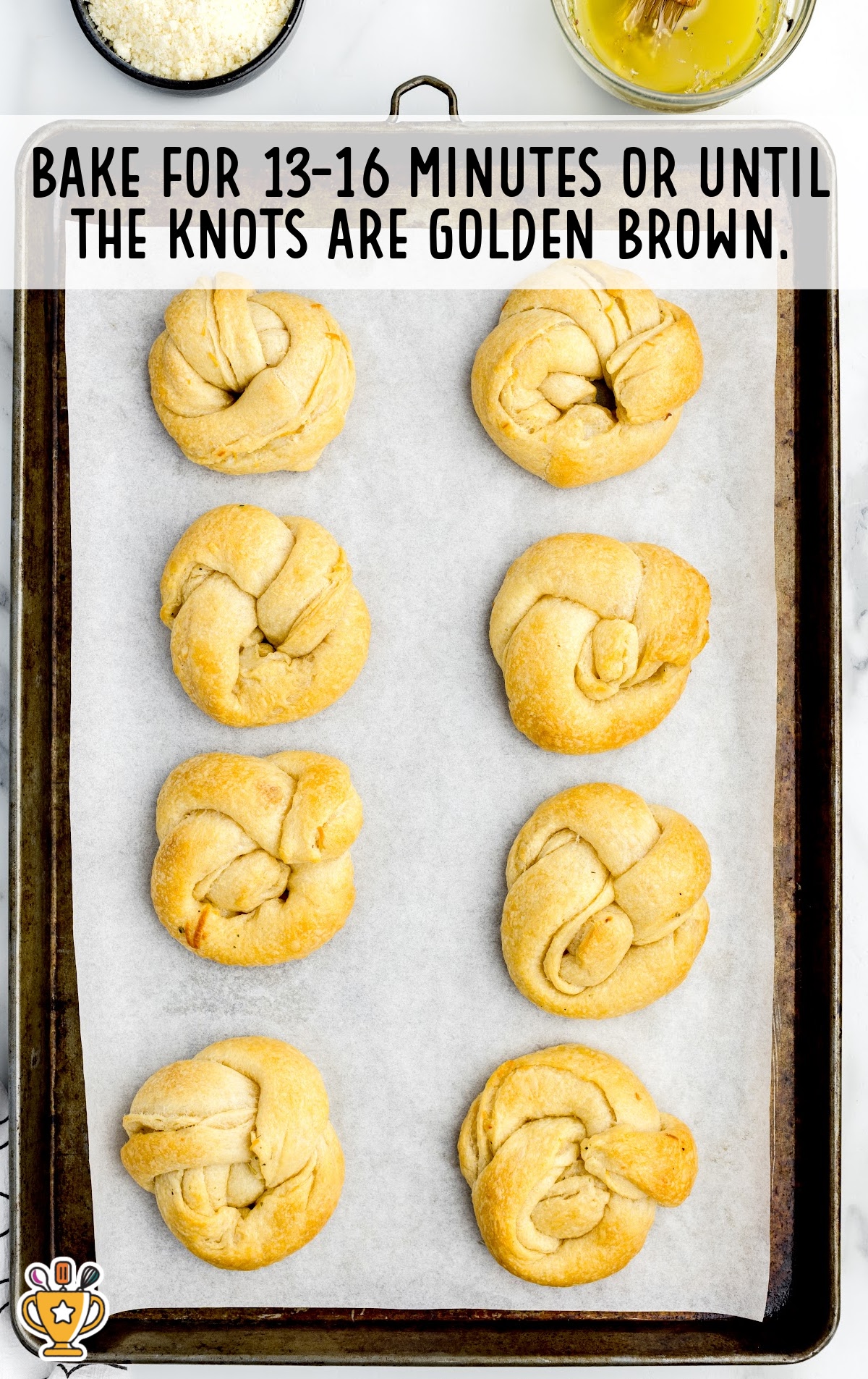 Baked garlic knots on a parchment-lined baking sheet, golden brown and ready to be brushed with butter and seasoning.