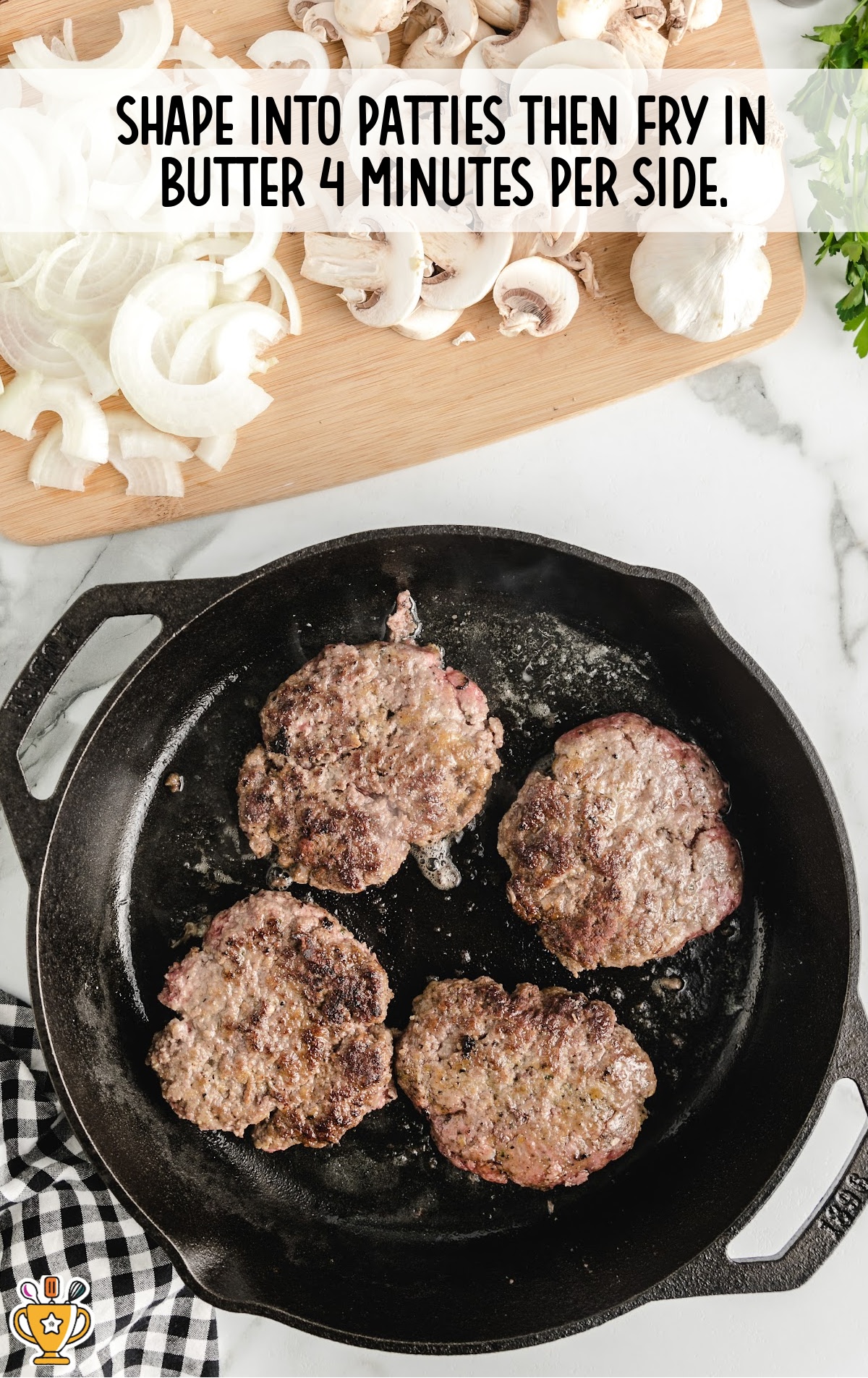 Four ground beef patties frying in a cast iron skillet with butter, next to a cutting board topped with sliced onions and mushrooms.
