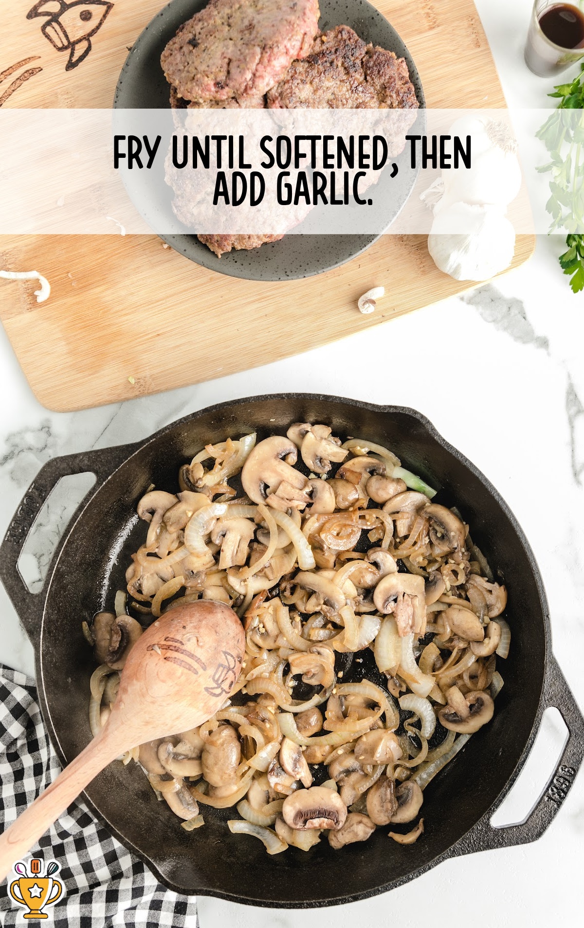 Cooked onions and mushrooms softening in a skillet with a wooden spoon, with garlic about to be added.