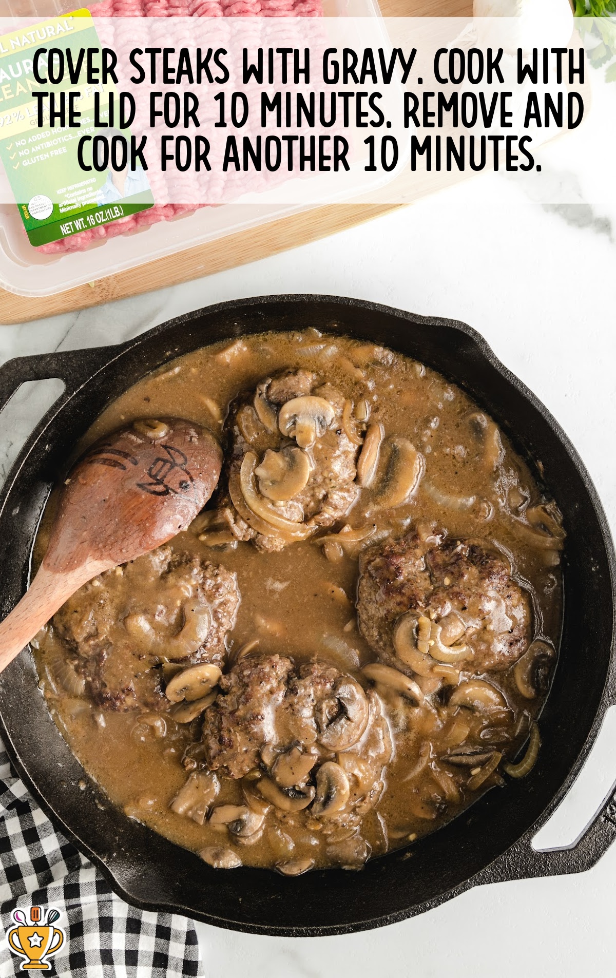 Gravy-covered hamburger steaks simmering in a skillet with sliced mushrooms and onions, finishing the cooking process.