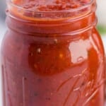 Close-up of homemade tomato sauce in mason jars, with rich red color and visible herbs and seasonings.