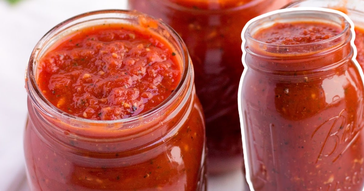 Close-up of mason jars filled with homemade tomato sauce, showing thick texture and speckled herbs throughout.