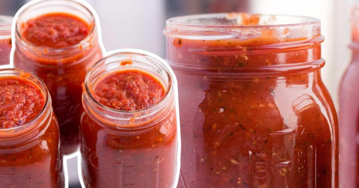 Three mason jars filled with thick, chunky homemade tomato sauce with visible spices, on a white background.