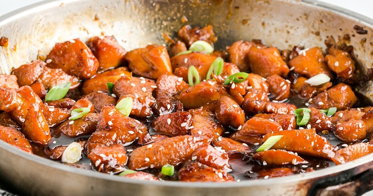 Side view of saucy honey garlic chicken in a skillet, garnished with sesame seeds and chopped green onions.