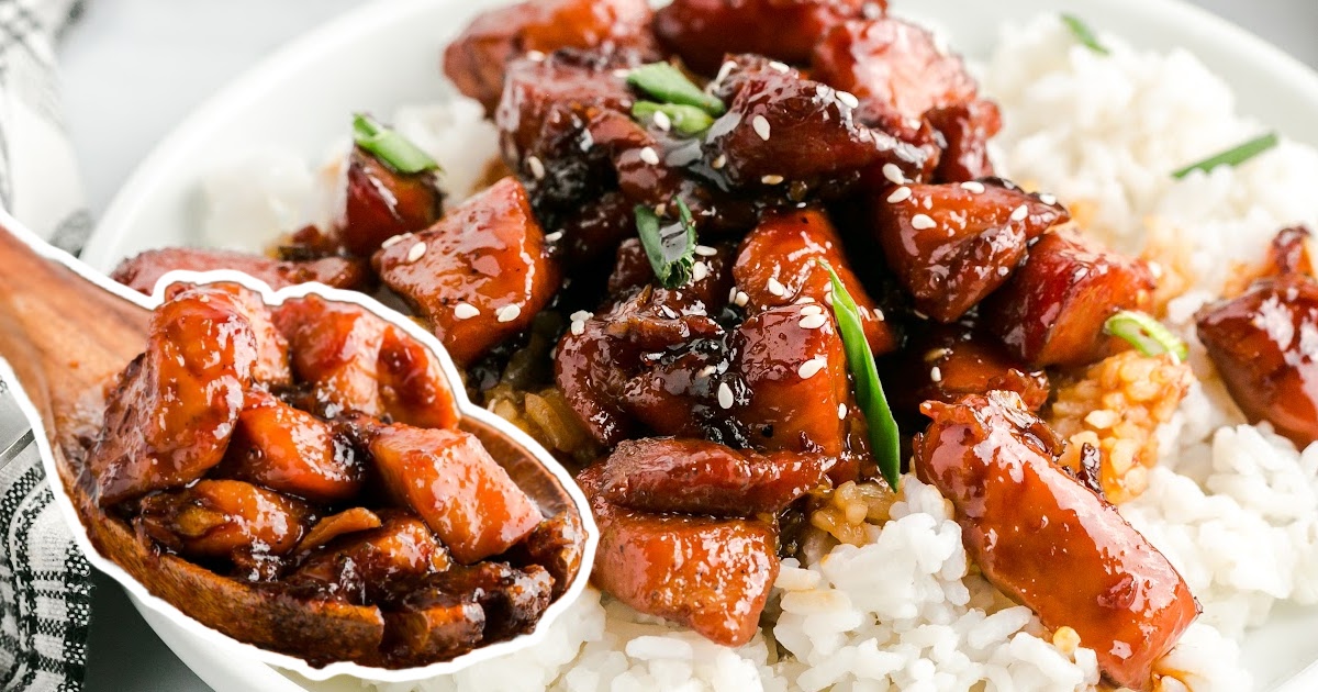 Close-up view of sticky honey garlic chicken pieces garnished with sesame seeds and chopped green onions served over white rice.
