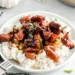 Plate of honey garlic chicken served over fluffy white rice, topped with sesame seeds and chopped green onions.