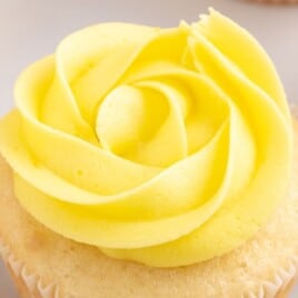 Close-up of a cupcake topped with piped lemon buttercream frosting, surrounded by lemon slices.