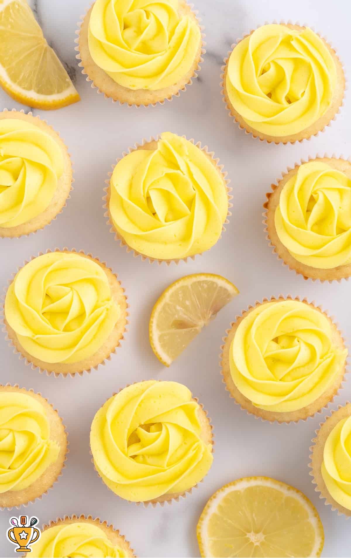 Overhead shot of cupcakes topped with rosettes of lemon buttercream frosting with lemon wedges around them.