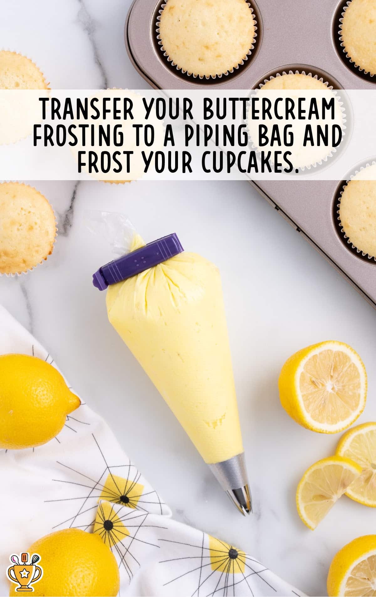 Piping bag filled with lemon buttercream frosting ready to decorate cupcakes, surrounded by lemons and cupcakes in a tin.