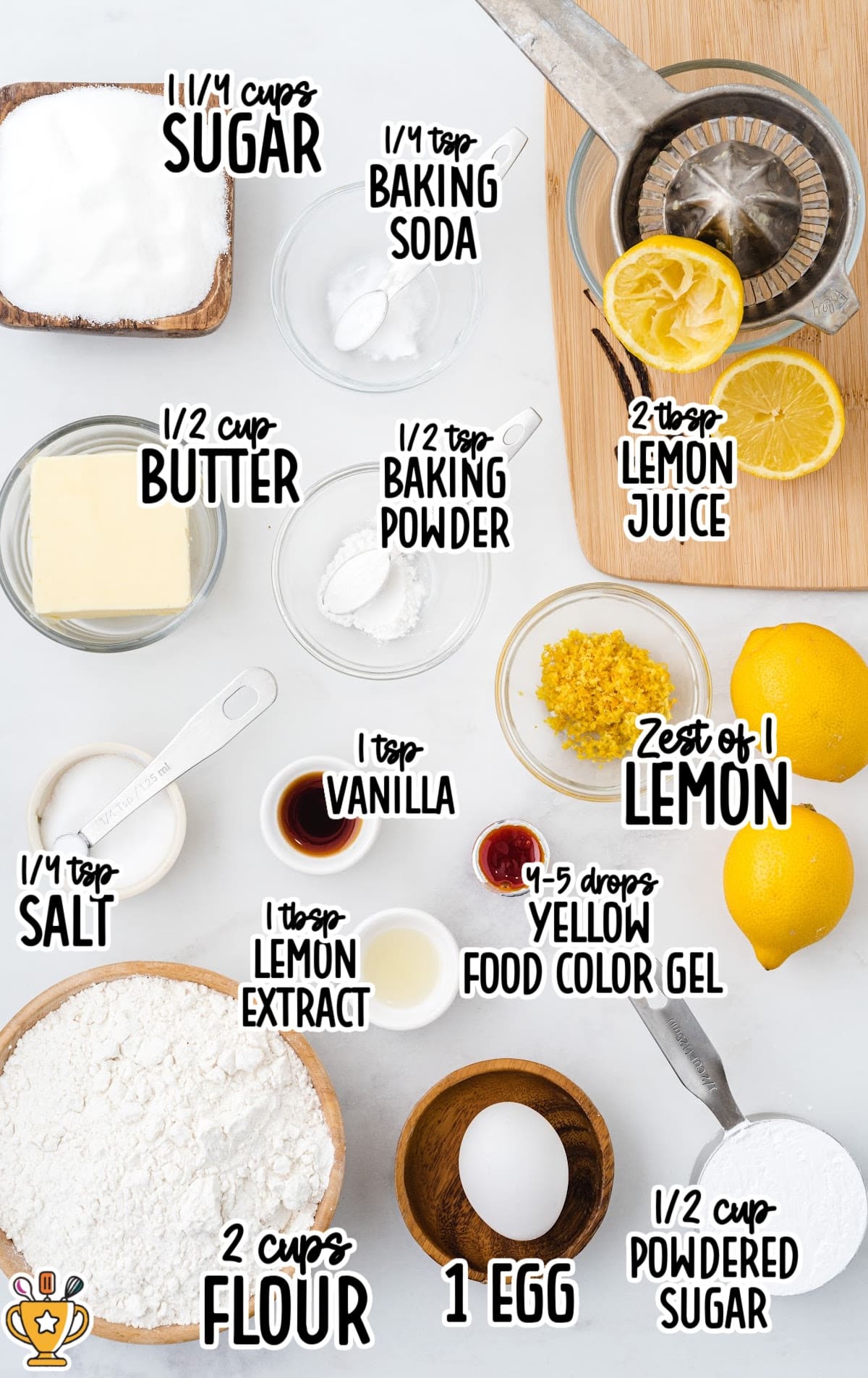 Overhead view of all labeled ingredients for lemon crinkle cookies arranged on a white surface with lemons and a juicer.