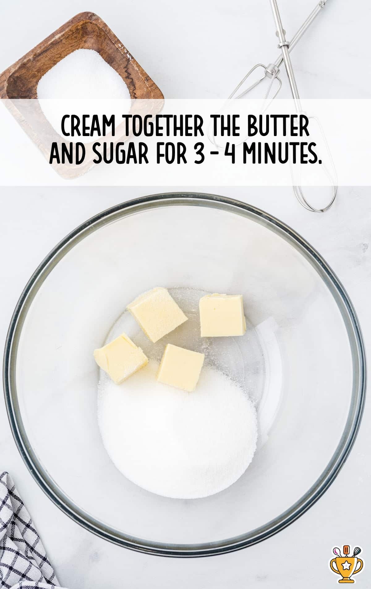 Butter and sugar in a mixing bowl ready to be creamed, with beaters and a wooden bowl of sugar nearby.