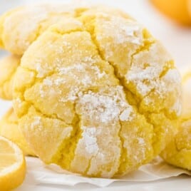 Close-up view of lemon crinkle cookies, dusted with powdered sugar, surrounded by lemon slices and soft background lighting.