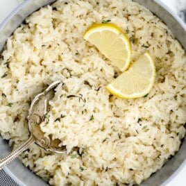 Overhead shot of a large pot filled with lemon rice, garnished with fresh thyme and lemon slices, with a silver serving spoon resting inside.
