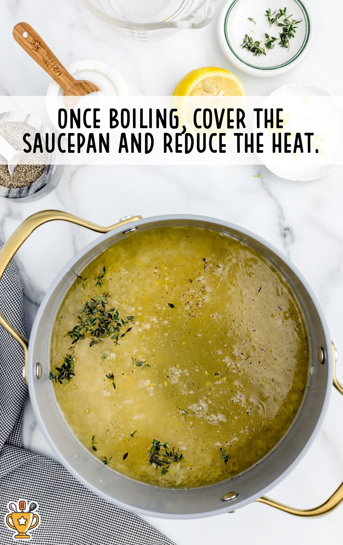 Lemon rice cooking in broth with thyme and pepper; pot is starting to boil on a marble counter with lemon halves and salt nearby.