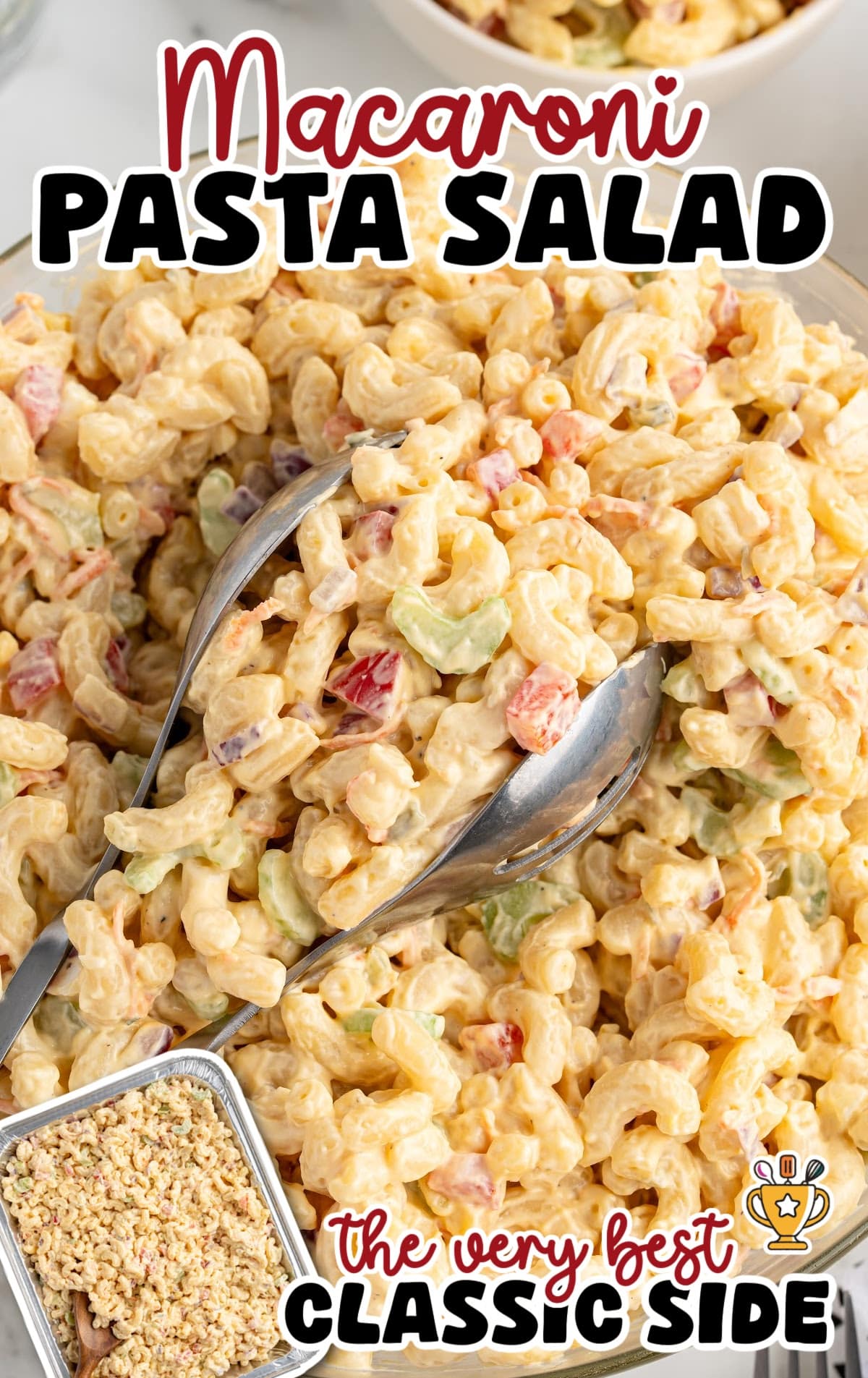 Close-up of creamy macaroni pasta salad with diced celery, red pepper, and onions in a thick dressing, served with metal tongs.