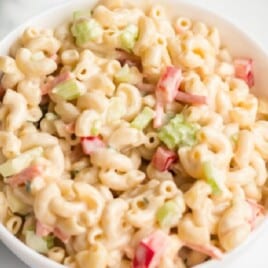 Overhead shot of macaroni salad in a white bowl on a marble surface, with diced vegetables mixed into the pasta.