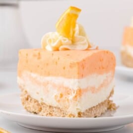 Side view of a bright and fluffy slice of orange creamsicle cake, layered with orange and cream filling, served on a white plate.