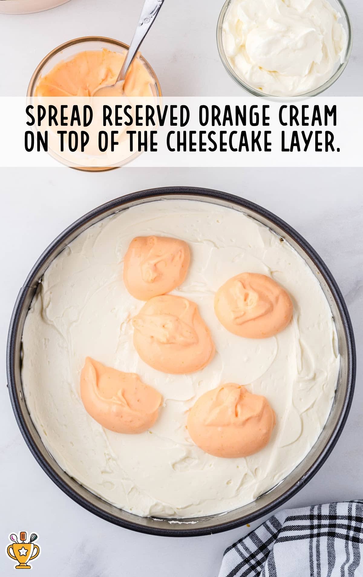 Glass bowls filled with orange cream and whipped cream next to a springform pan layered with creamy cheesecake, topped with dollops of orange cream.