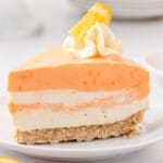 Recipe card with ingredients for no-bake orange creamsicle cheesecake arranged neatly on a counter, including orange zest, Jello, whipped cream, cream cheese, and more.
