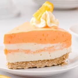 Recipe card with ingredients for no-bake orange creamsicle cheesecake arranged neatly on a counter, including orange zest, Jello, whipped cream, cream cheese, and more.