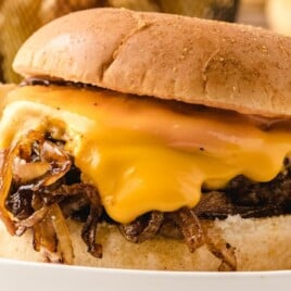 Side view of an onion burger topped with cheese and grilled onions, bun lifted slightly to reveal the juicy filling.