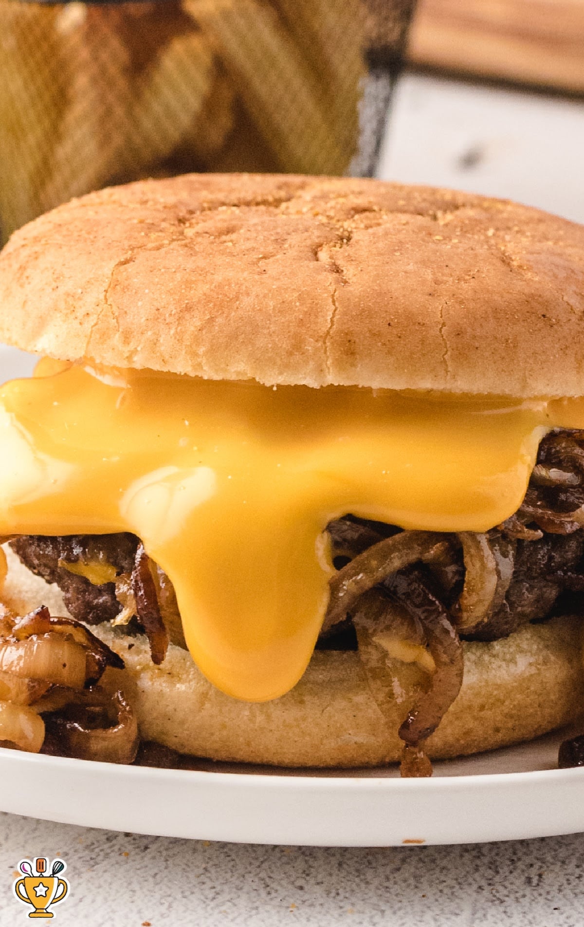Close-up of a juicy onion burger with melted American cheese dripping over grilled onions on a toasted bun.