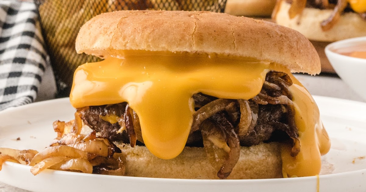 Delicious onion burger with a thick layer of melted cheese and grilled onions, placed on a white plate.