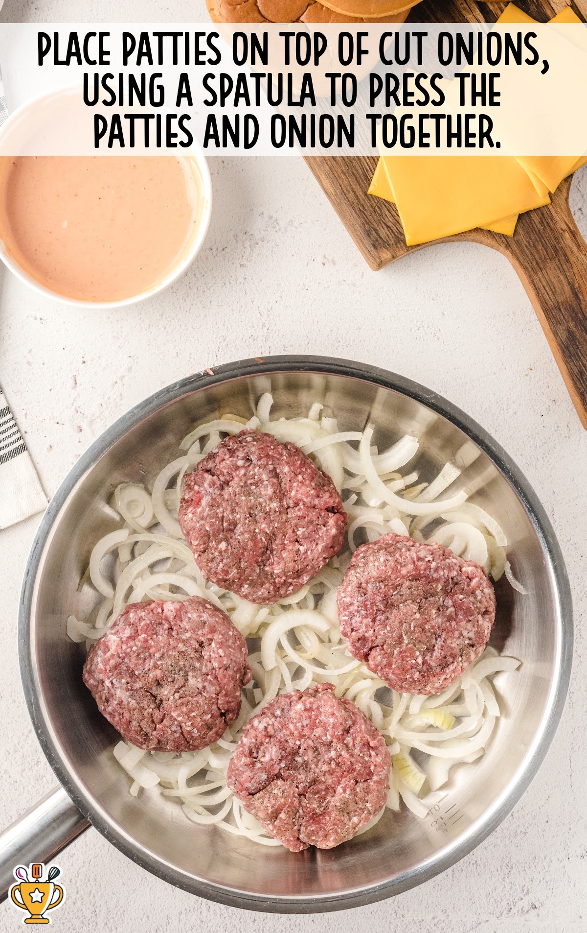 Uncooked beef patties placed on a bed of sliced onions in a skillet, ready to be pressed and fried.