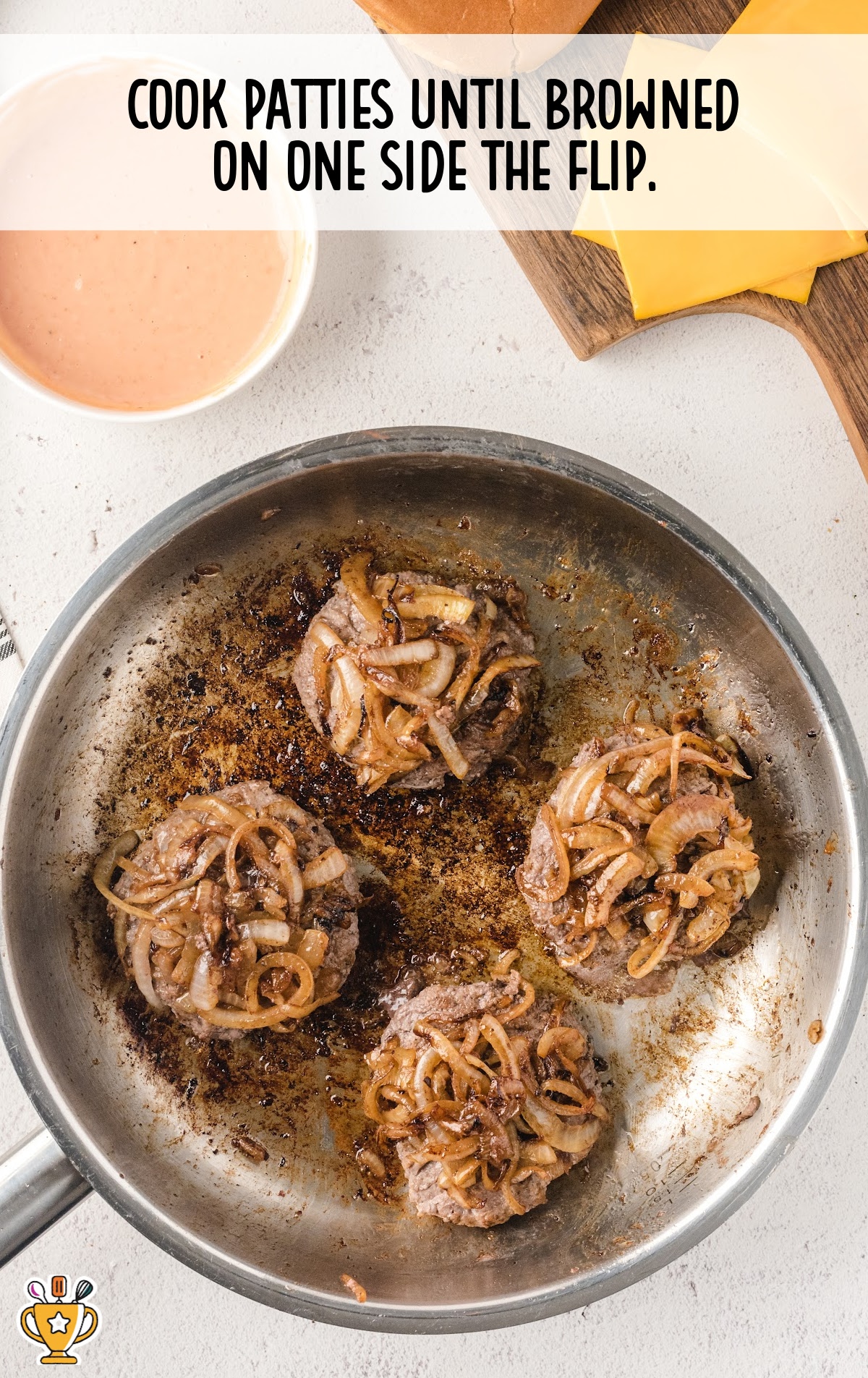 Burger patties with golden fried onions cooking in a skillet, nicely browned and sizzling in the pan.
