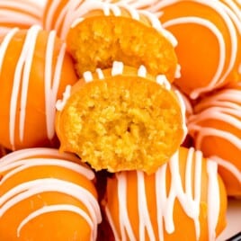 Orange truffles with candy coating and white drizzle arranged on a plate with one truffle bitten into, revealing its soft orange center.