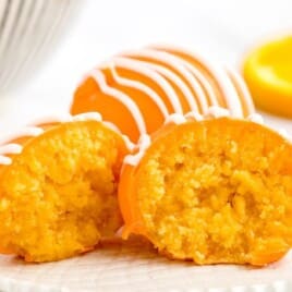 Close-up of a halved orange truffle with a moist, cake-like center and white drizzle on top, sitting on a white plate.