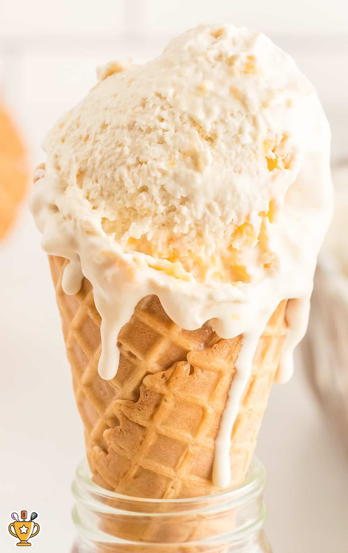 Peach ice cream scooped high in a waffle cone, dripping down the side, placed inside a glass jar.