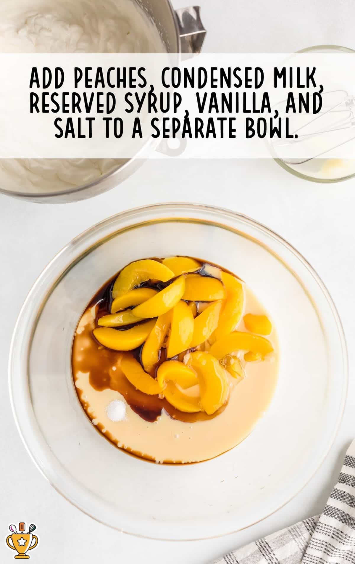 Overhead image of a glass bowl with sliced peaches, condensed milk, syrup, vanilla, and salt, ready to be mixed. Background shows whipped cream mixture in another bowl.