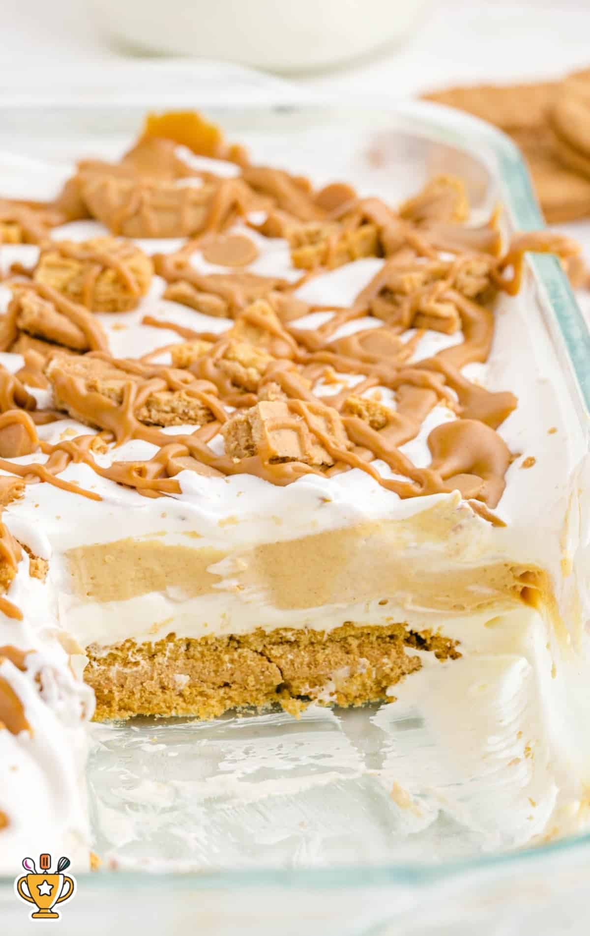 Side view of a glass dish filled with layered peanut butter lasagna showing crust, peanut butter layer, and whipped topping.