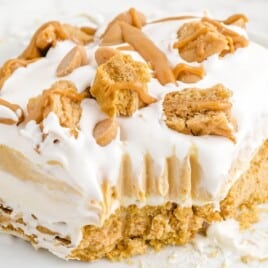 Close-up view of a creamy peanut butter lasagna slice with layers of whipped topping, peanut butter filling, and cookie crust on a white plate.