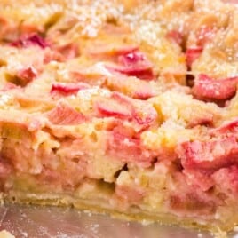 Half-sliced rhubarb custard pie in a metal pie tin, showing a creamy and vibrant rhubarb-studded interior.