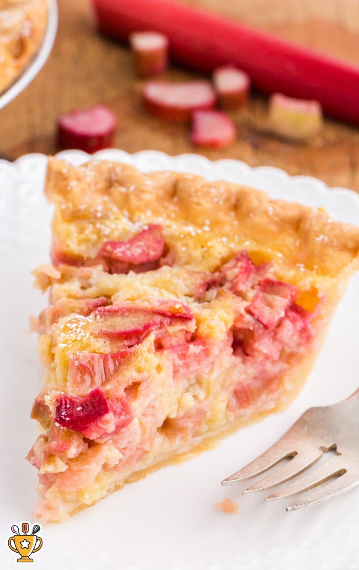 Single slice of rhubarb custard pie on a white plate with a fork beside it, showing the soft filling and crisp crust.