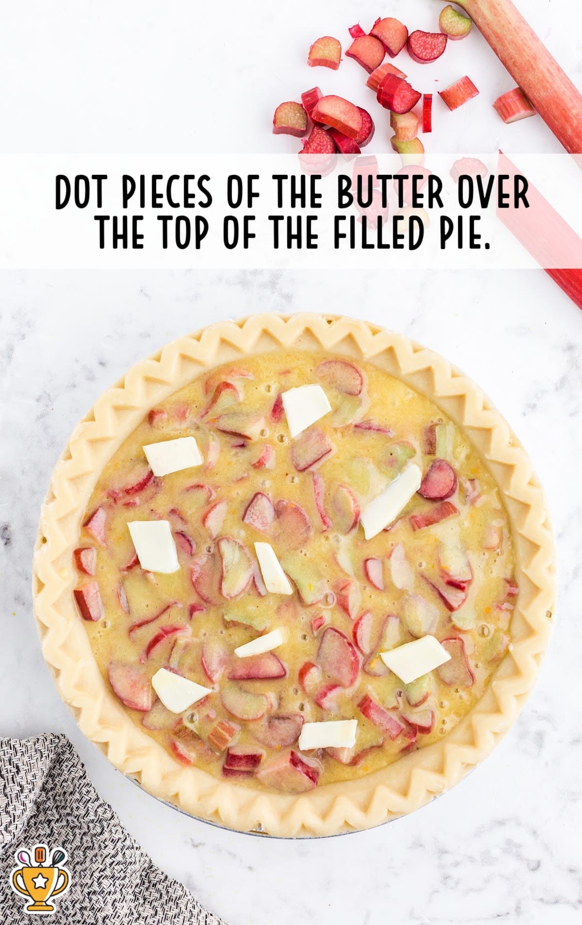 Unbaked rhubarb custard pie with pieces of butter dotted over the top of the custard filling.